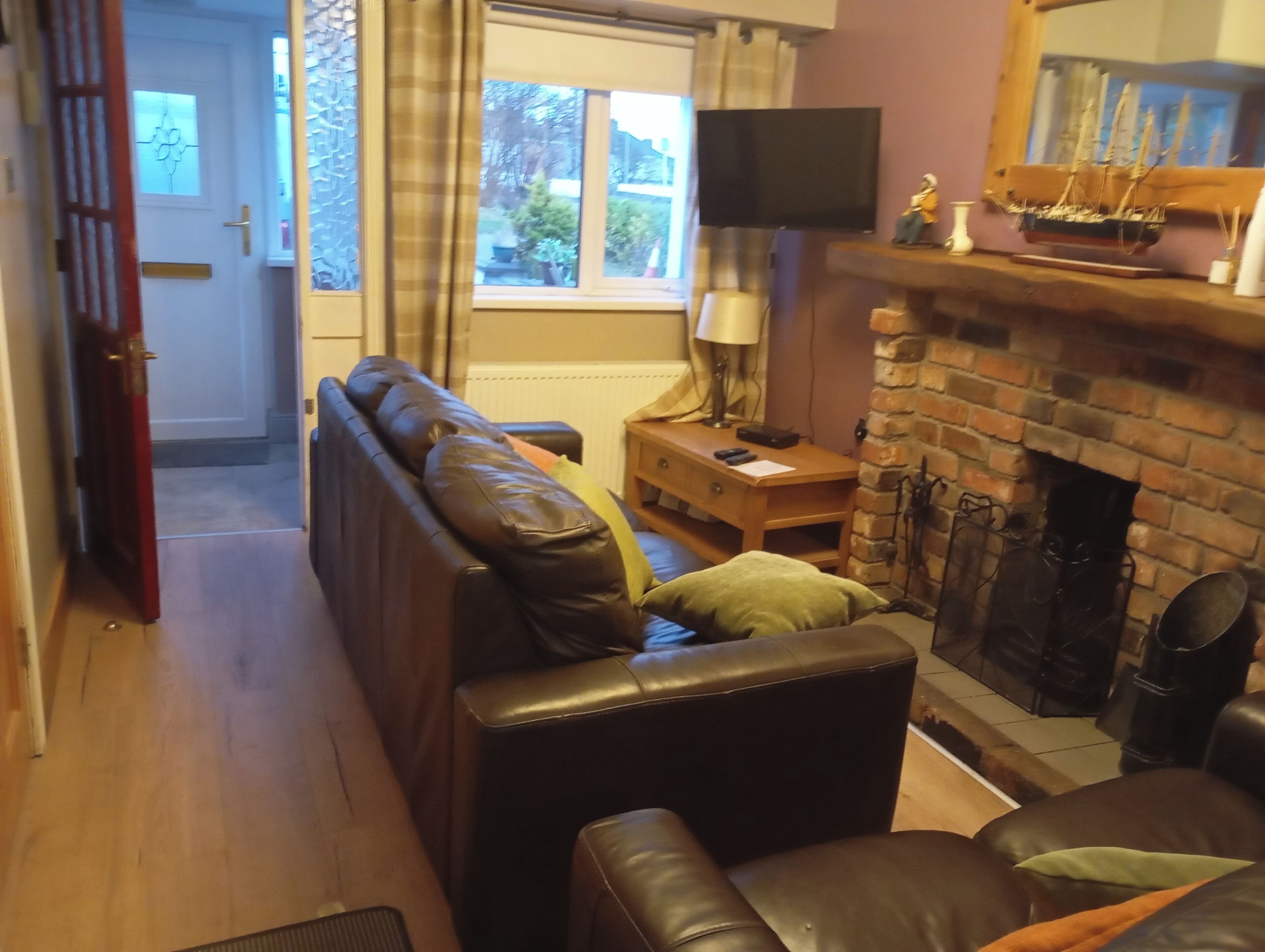 A living room with a leather sofa, a wooden side table, a fireplace, and a television.