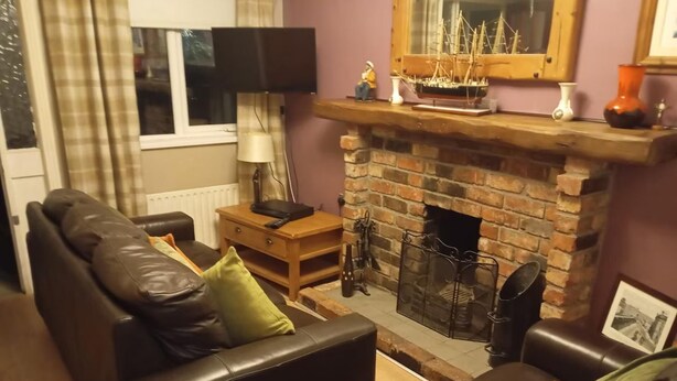 Una sala de estar con chimenea de ladrillo, sofás de cuero, una mesita de madera y un televisor.