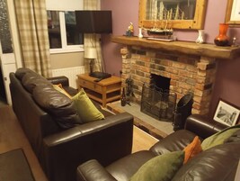 A living room with a brick fireplace, leather sofas, a wooden side table, and a television.