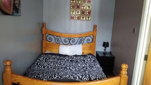Una cama con una colcha estampada, un cabecero de madera con detalles decorativos, un espejo montado en la pared y una mesita de noche con una lámpara.