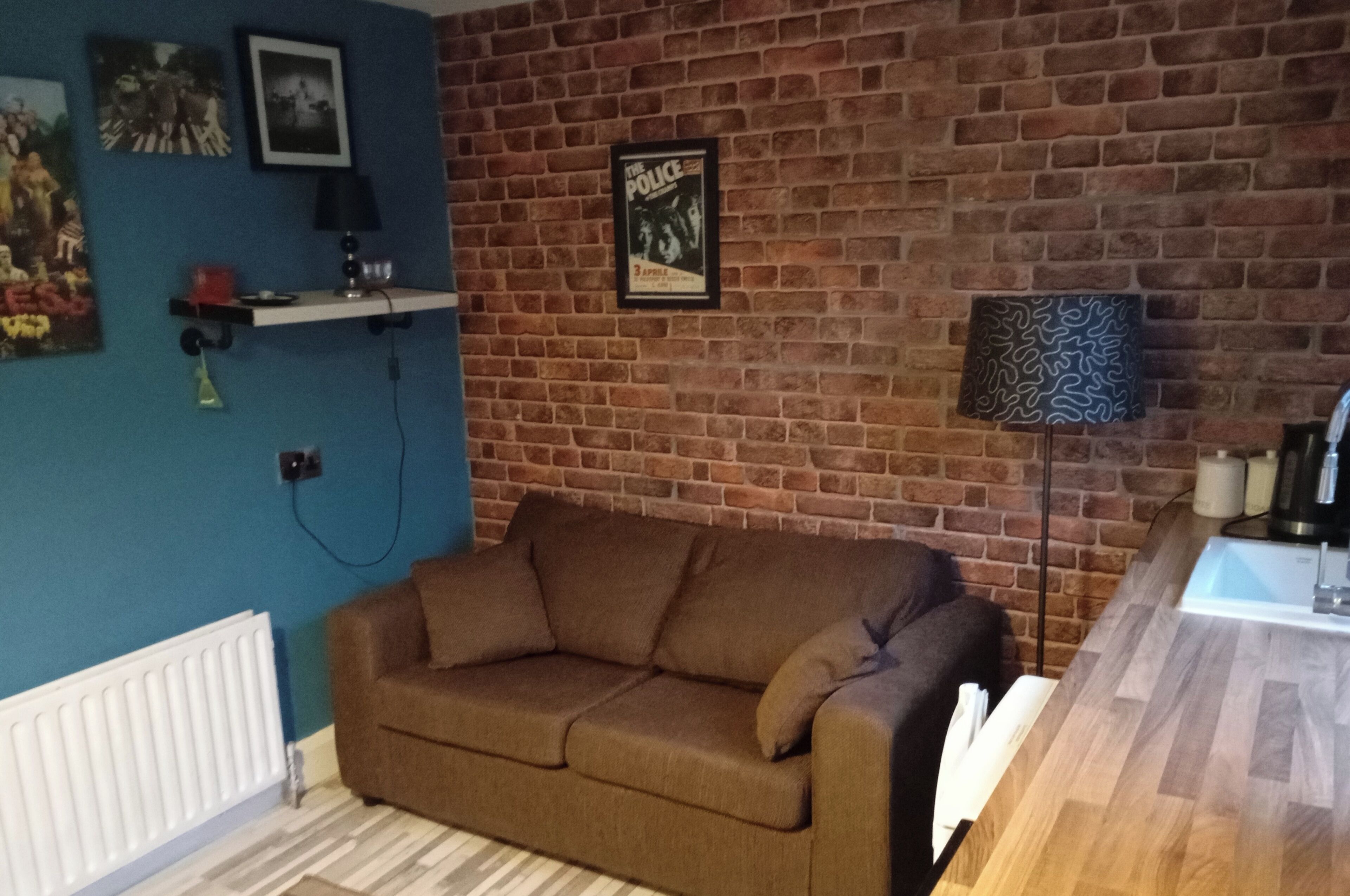 A living room with a brick wall, a blue wall, a brown sofa, a lamp, and a coffee table.