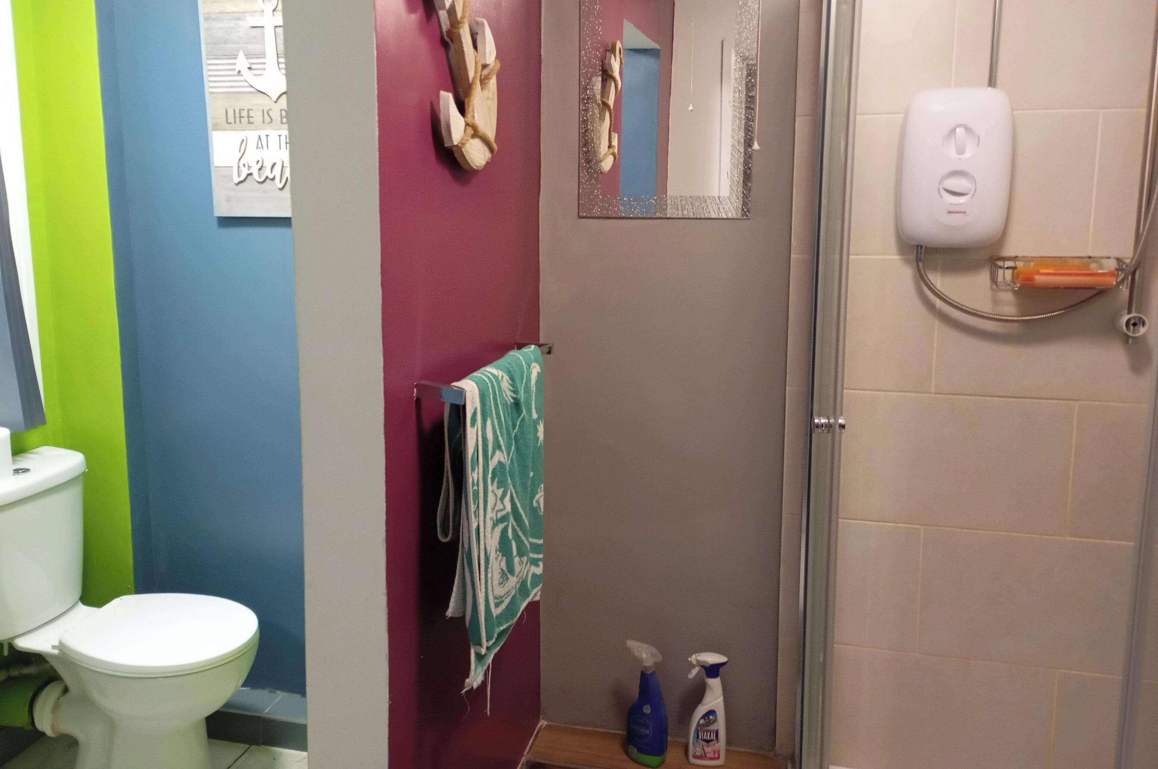 A bathroom with a toilet, a towel rack with a towel, a shower area, and a mirror.