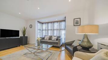 A modern living room with a flat-screen TV, a sofa, a coffee table, and a lamp.