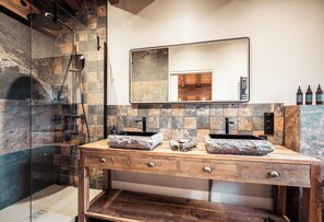 Een moderne badkamer met een douchecabine van glas, twee wastafels met stenen aanrechtbladen, een houten wastafelmeubel en een grote spiegel.
