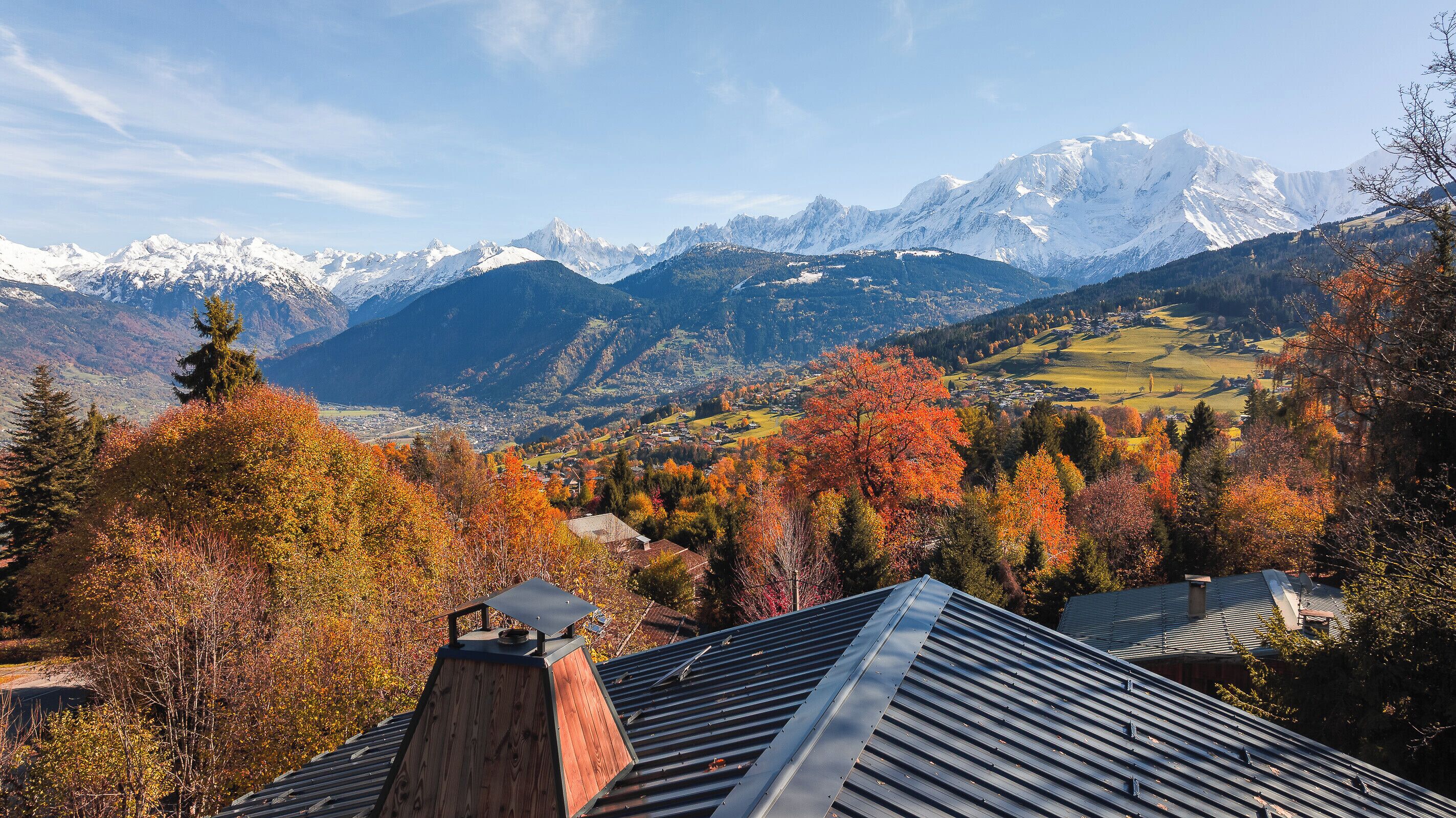 A mountain landscape with autumn foliage and snow-capped peaks in the background.