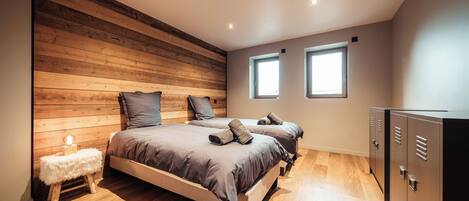 A bedroom with two beds, wooden paneling on one wall, a small stool, and a wardrobe.