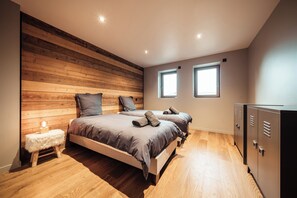 Een slaapkamer met twee bedden, houten lambrisering aan een wand, een klein krukje en een garderobe.