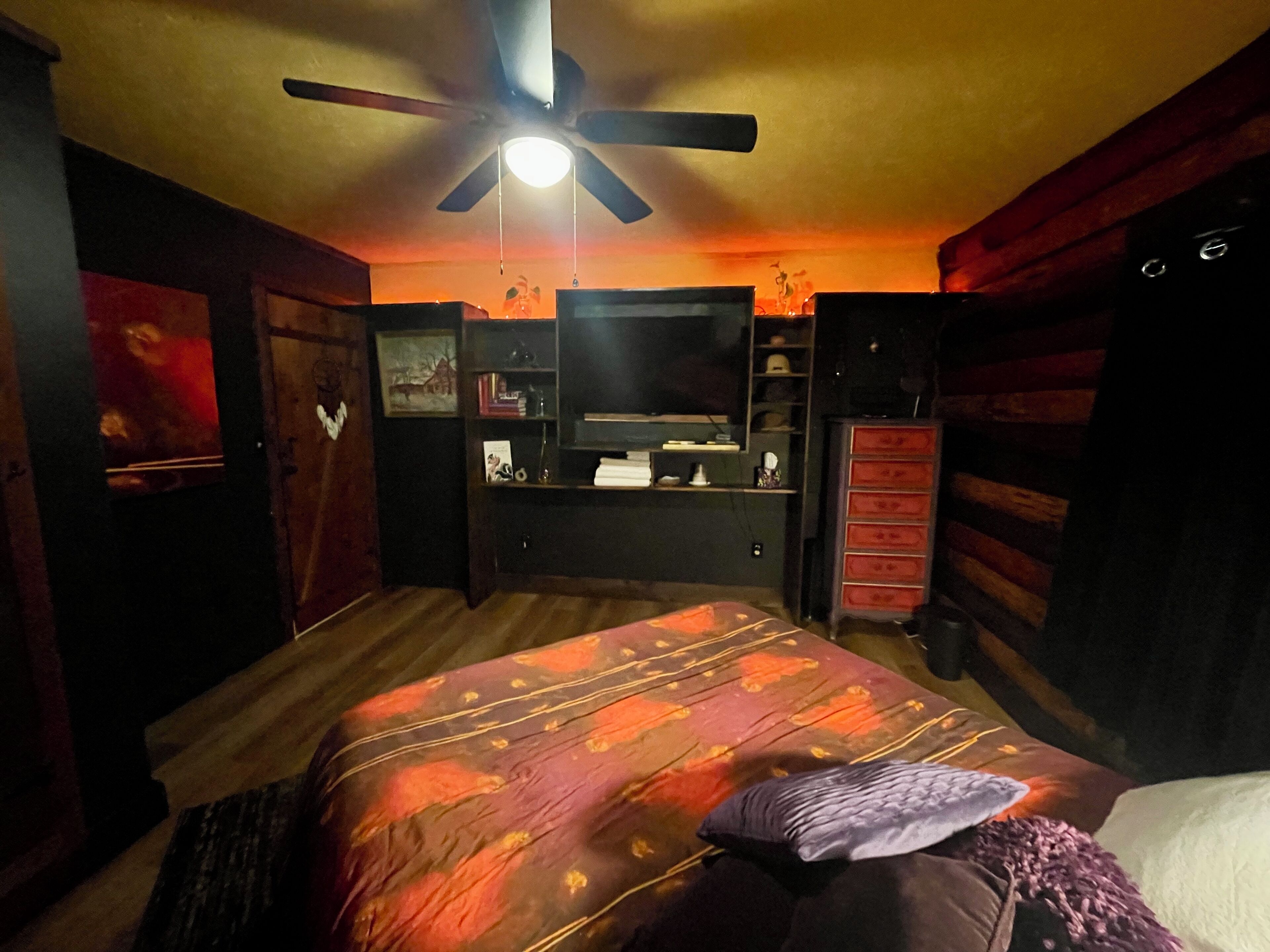 A bedroom with a bed, a ceiling fan, a dresser, and a TV stand.