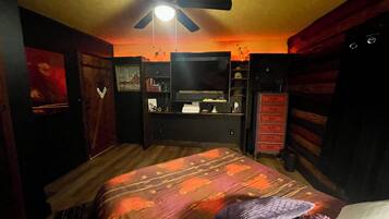 A bedroom with a bed, a ceiling fan, a dresser, and a TV stand.