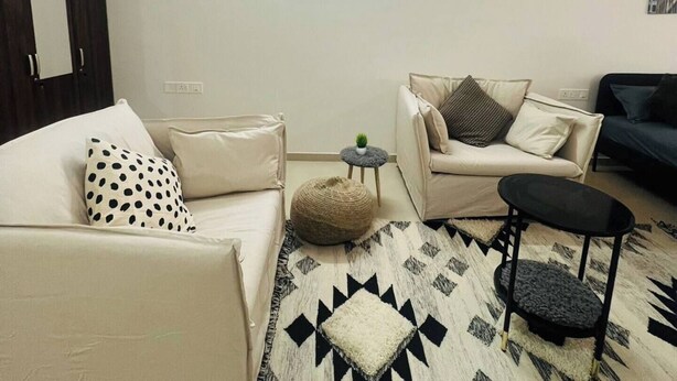 Una sala de estar con ventilador de techo, sofá, una mesa de centro y un tapete estampado.