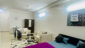 Habitación bien iluminada con una cama, un escritorio y una silla. Incluye un ventilador de techo y un reloj de pared.