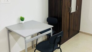 Una habitación pequeña con una mesa blanca, dos sillas negras, un reloj, un armario y una planta pequeña.