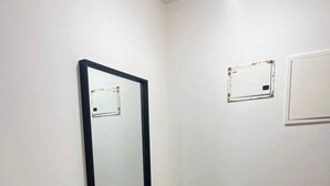 Un rincón de una habitación con un espejo grande, una planta en maceta y dos interruptores de luz en la pared.