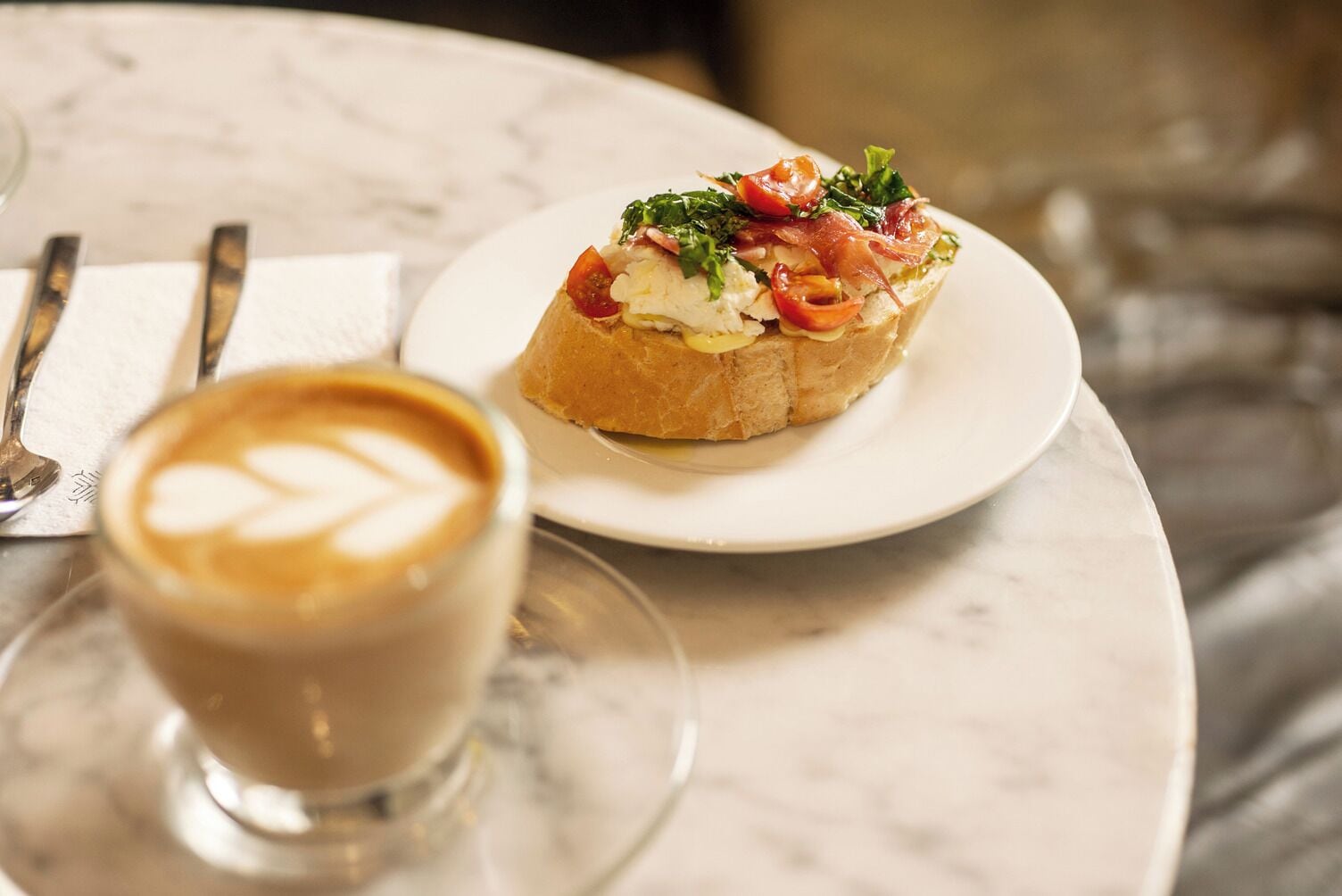 Een bord bruschetta met toppings en een kop koffie op een marmeren tafel.