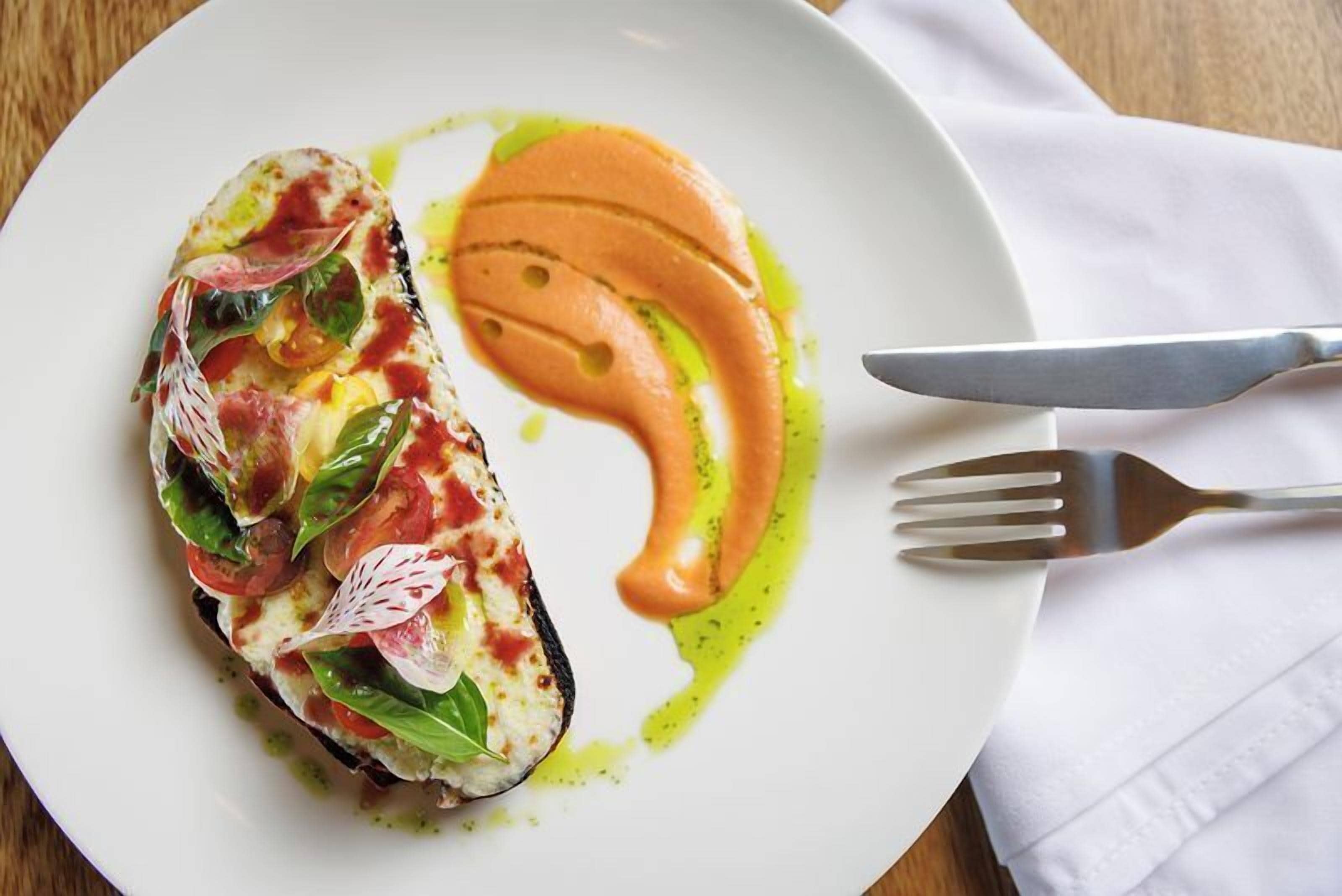 A plate with a grilled vegetable dish, a fork, and a knife on a white napkin.