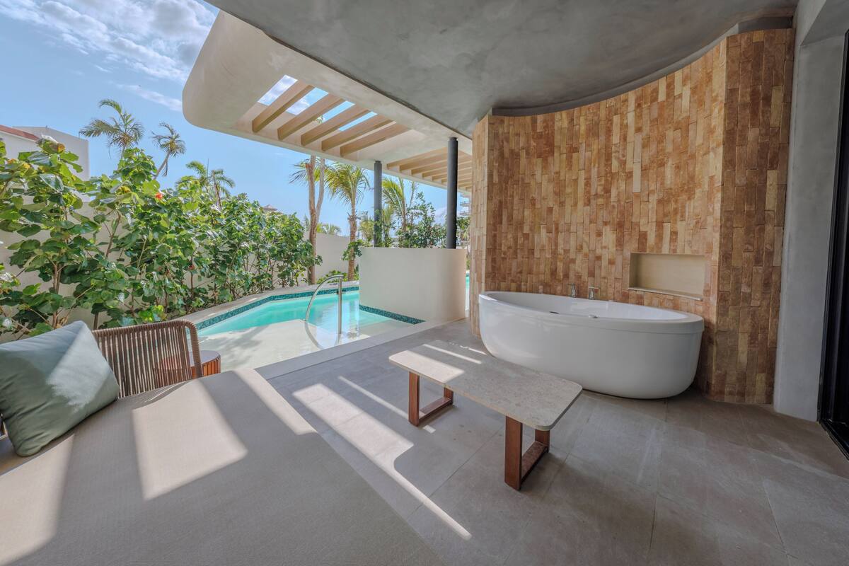 Ein modernes Badezimmer mit einer freistehenden Badewanne, einer Sitzbank und Blick auf einen Pool.