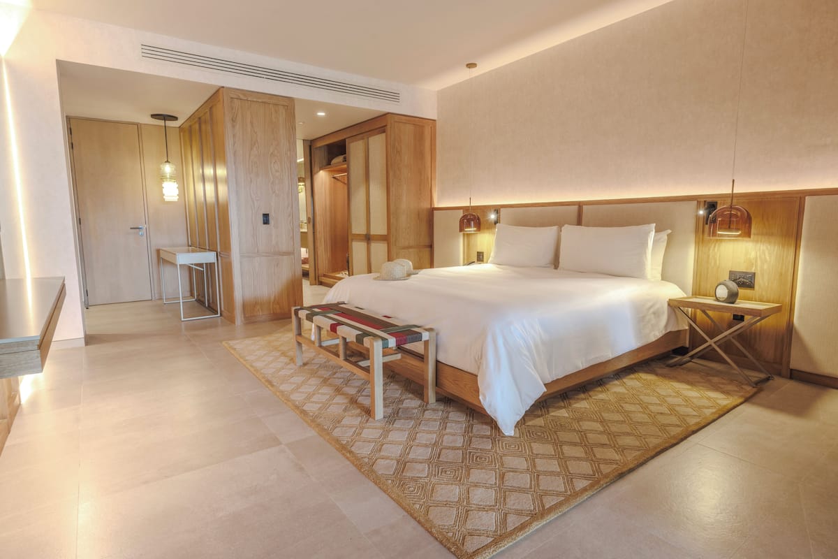 Ein modernes Hotelzimmer mit einem großen Bett, Nachttischen, einer Bank und einem begehbaren Kleiderschrank.