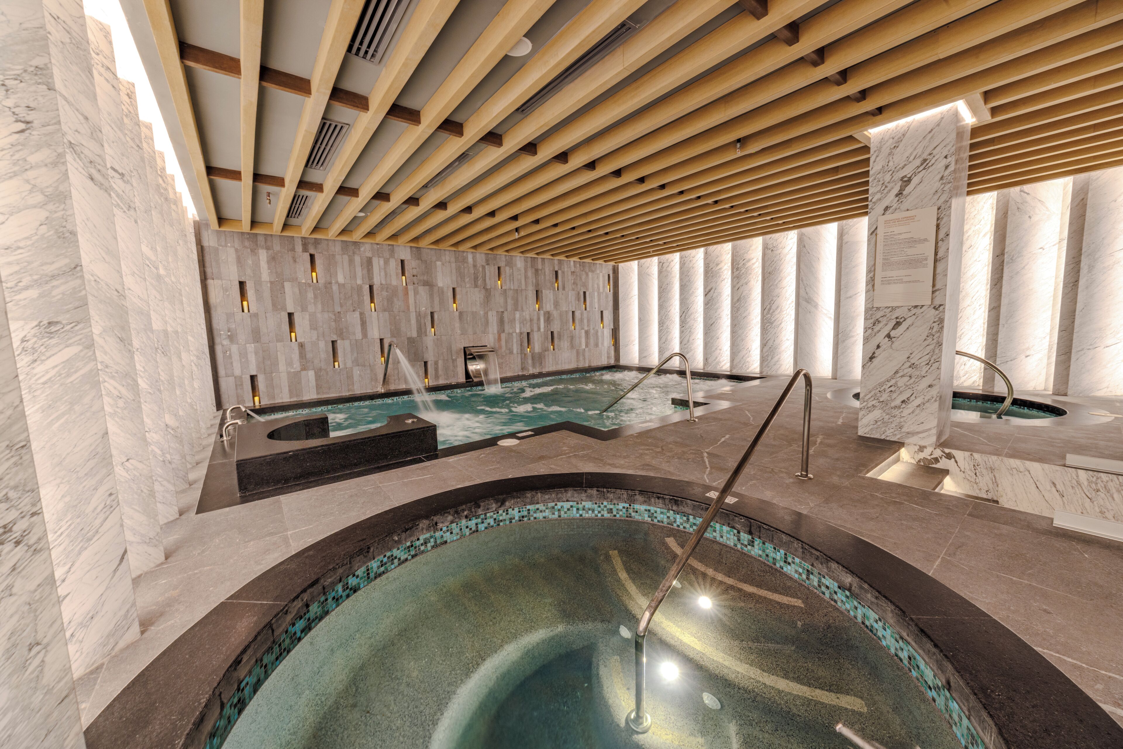 A spa area with a large hot tub and a smaller pool, wooden ceiling beams, and marble walls.