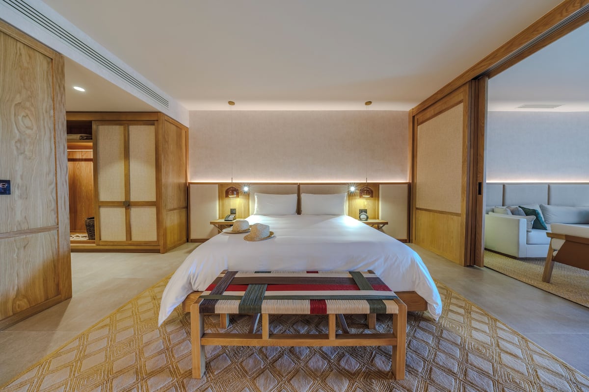 Ein geräumiges Schlafzimmer mit einem großen Bett, Nachttischlampen, einer Holzbank und Blick auf einen Balkon.