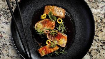 Un plato negro con comida, incluyendo salmón y verduras, sobre una encimera de granito.