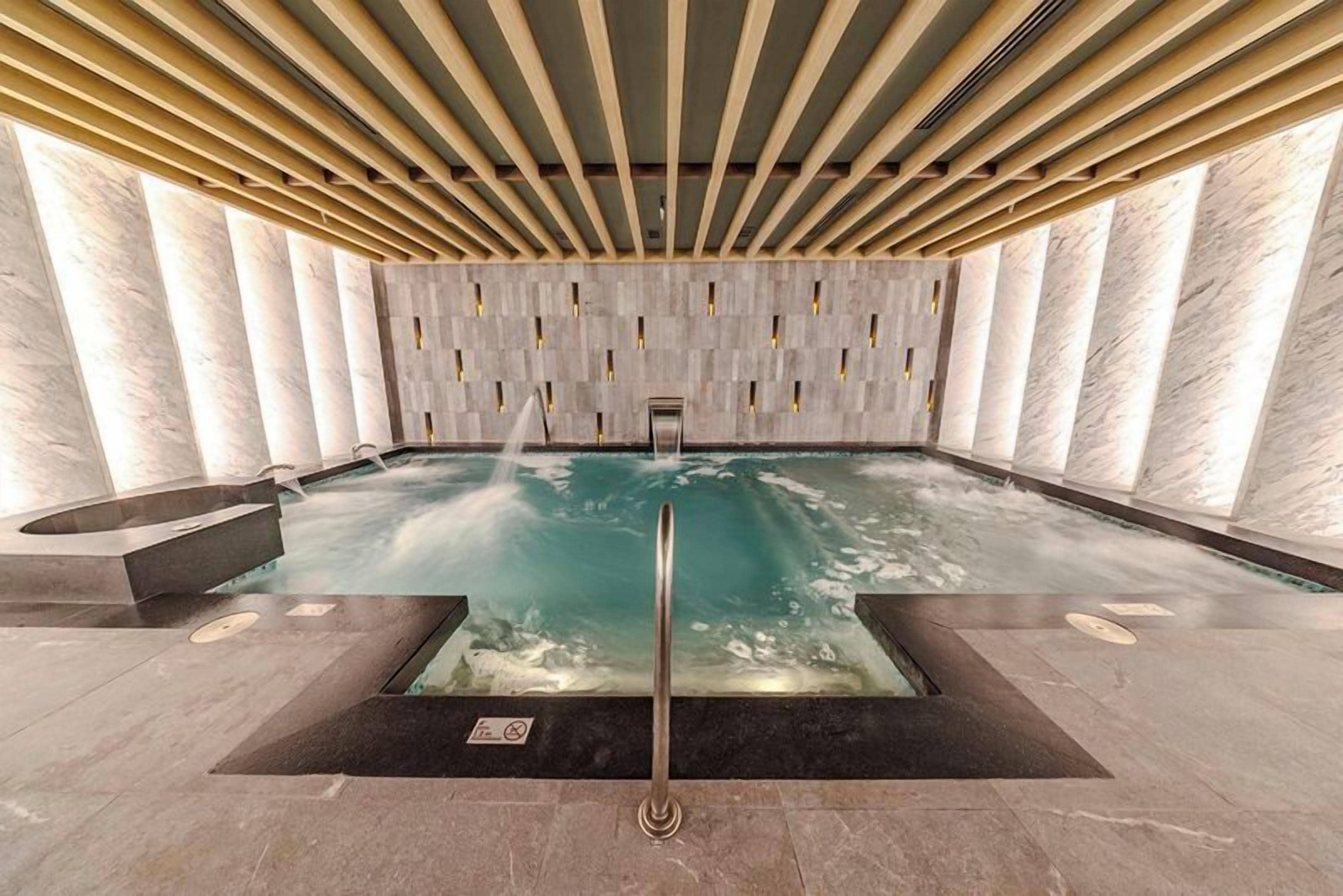 A modern indoor pool with a wooden ceiling and marble walls.