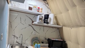 Una cocina compacta con un lavamanos, un microondas y una cafetera sobre una estantería.