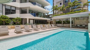 Un hotel moderno con zona de piscina, tumbonas y mobiliario de exterior.