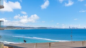 Vista costera con playa, océano y el perfil distante de una ciudad.