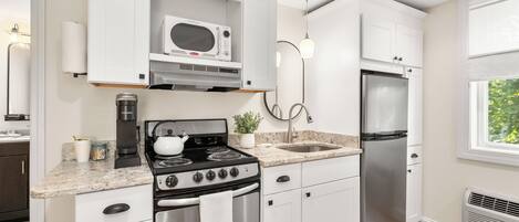 A modern kitchen with white cabinets, a stainless steel stove, a microwave, and a refrigerator.