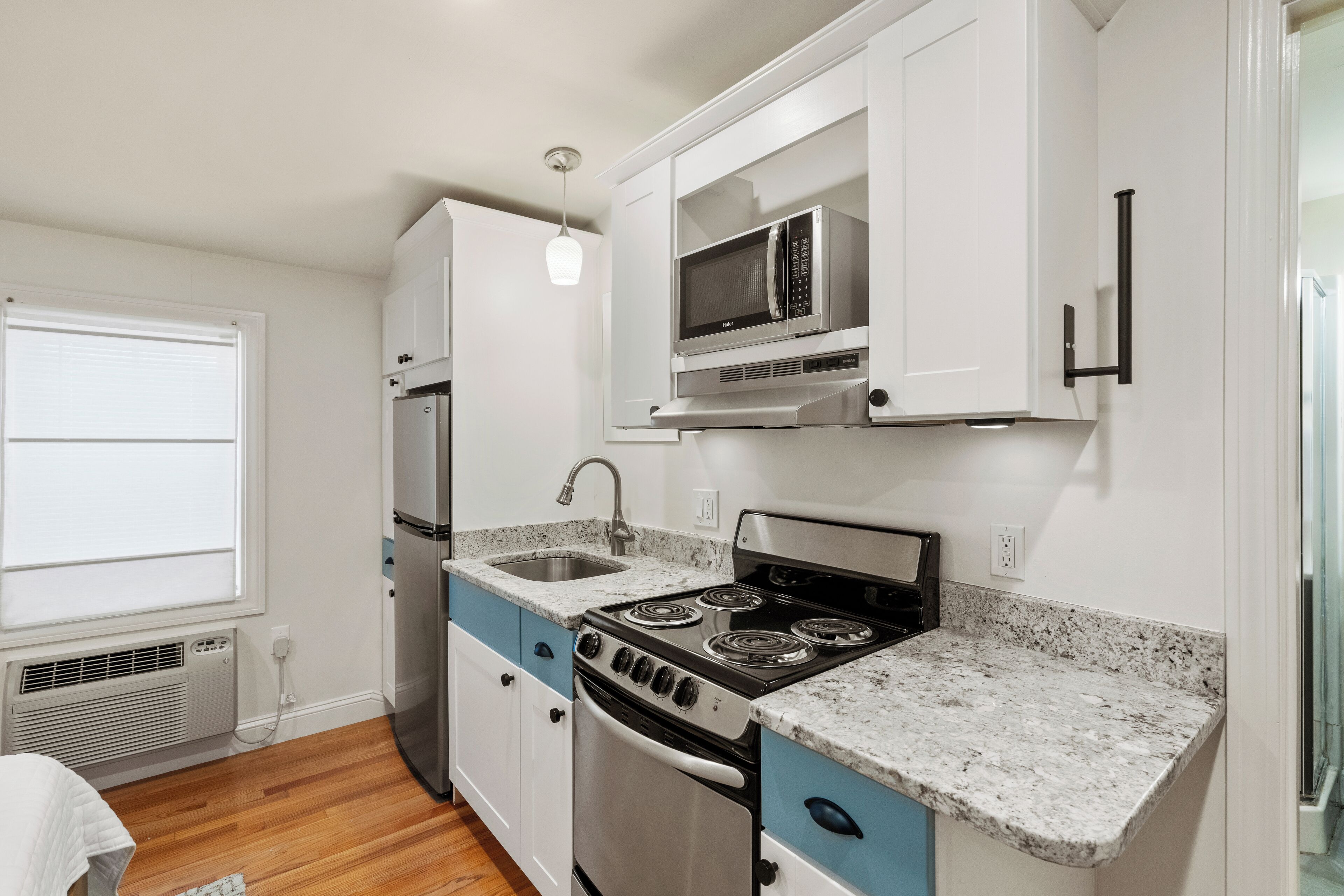 A compact kitchen with white cabinets, a stainless steel stove, a microwave, and a sink.