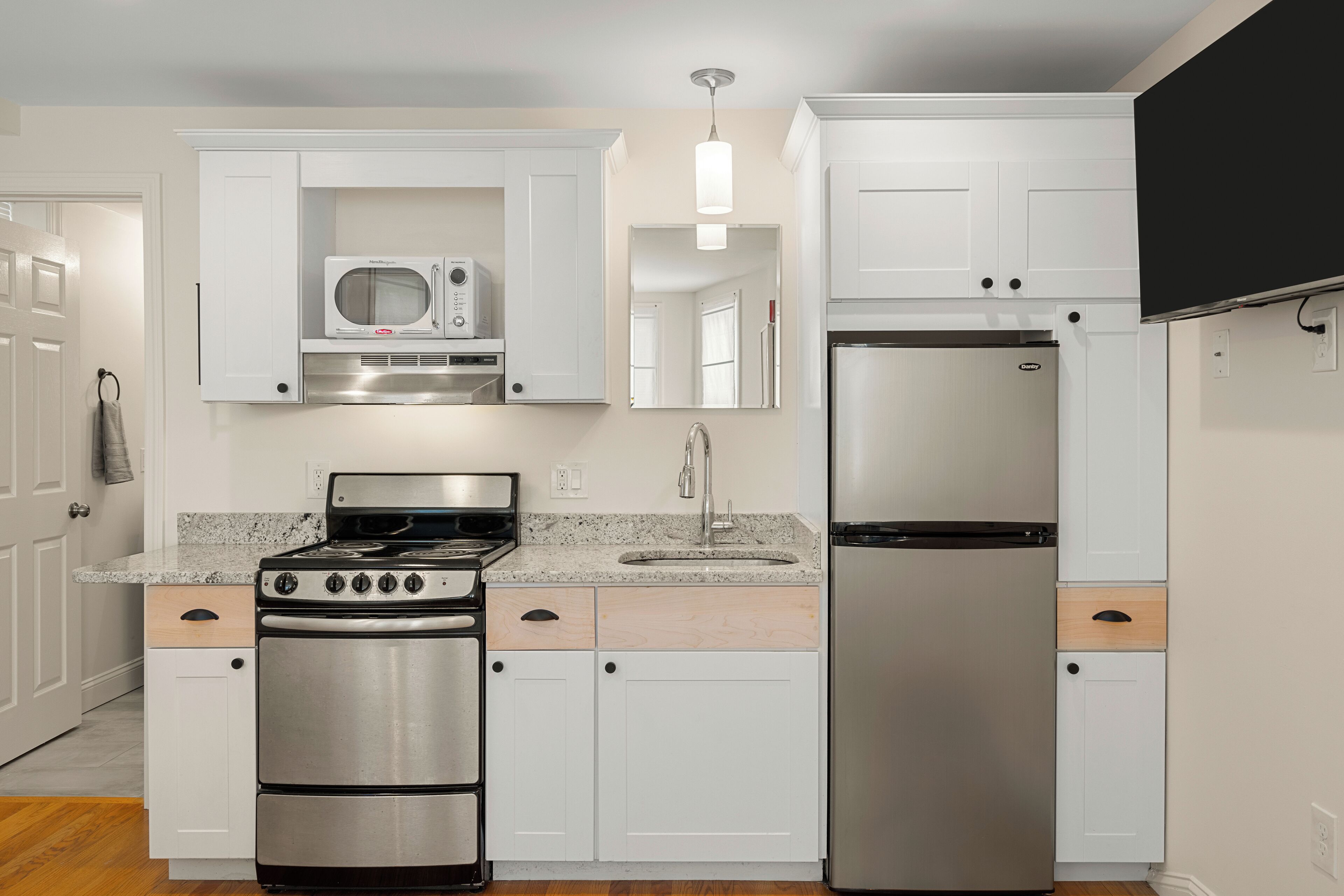 A modern kitchen with white cabinetry, a stainless steel stove, a refrigerator, and a microwave.
