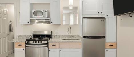 A modern kitchen with white cabinetry, a stainless steel stove, a refrigerator, and a microwave.