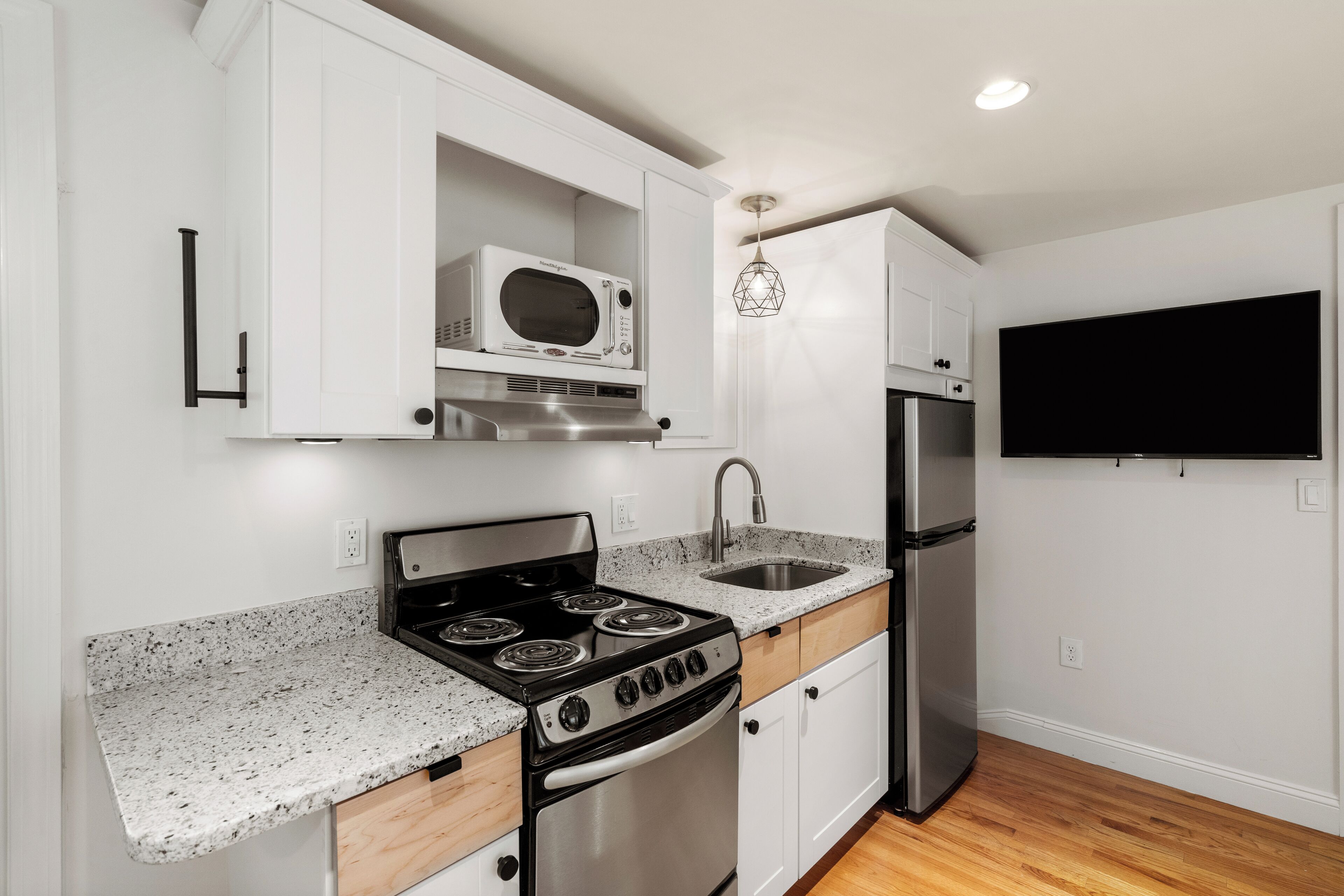 Una cocina con gabinetes blancos, encimera de granito, estufa, microondas, pileta y refrigerador.