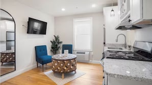 A compact kitchen with a stove, sink, and a round table with chairs. - Hygge House Suites (Newburyport)
