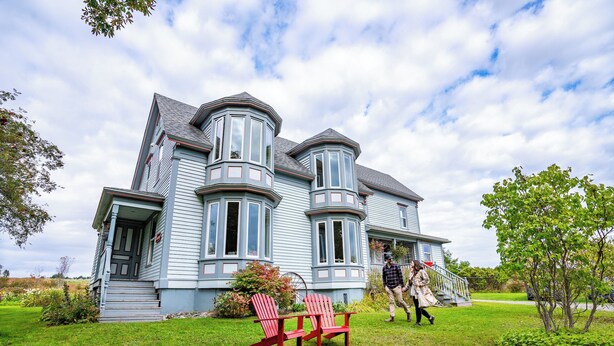 Une grande maison bleu clair, dotée d’une véranda qui fait le tour de la maison et d’une baie vitrée.