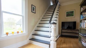 Un escalier avec des balustrades blanches et des marches noires, une bibliothèque remplie de livres et un téléviseur posé sur un meuble.