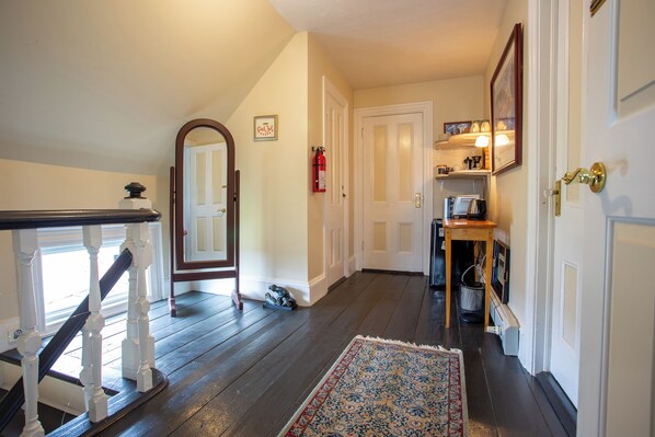 A hallway with a wooden staircase, a rug, and a door leading to another room.