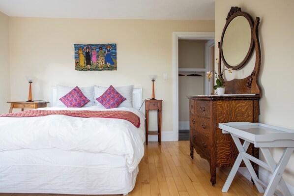 A bedroom with a large bed, a dresser, a mirror, and a painting on the wall.