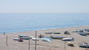 A beach with several boats parked on the sand, a lifeguard stand, and a person sitting under an umbrella. - Villas del Golf townhouse 27 (Manilva)