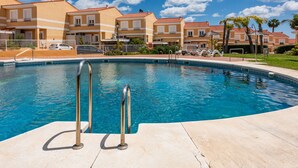 A swimming pool with metal ladders, surrounded by a poolside area with lounge chairs and a clear blue sky. - Villas del Golf townhouse 27 (Manilva)