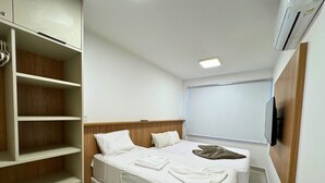 A hotel room with a bed, a TV mounted on the wall, and a wardrobe with shelves. - Studio Design 3 Apt 902 (Maceio)