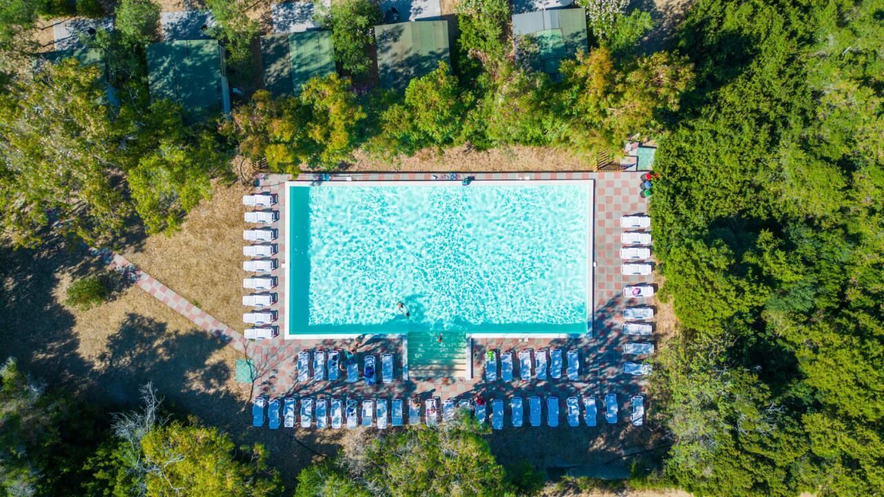 An aerial view of a rectangular swimming pool surrounded by lounge chairs and a row of parked cars.