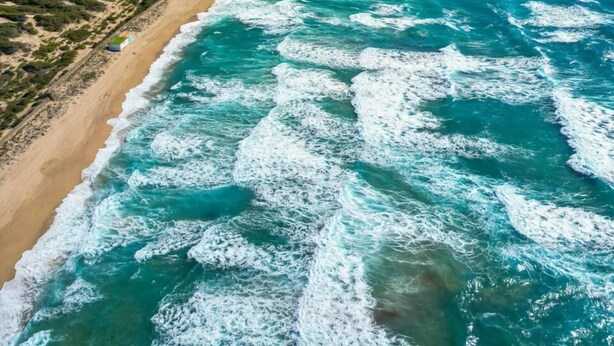 An aerial view of a coastal area with a long stretch of beach and ocean waves.