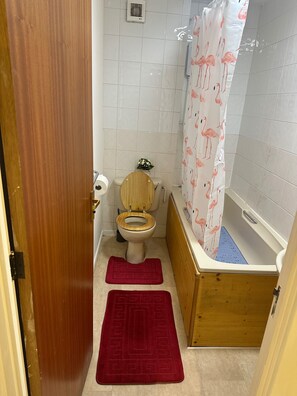 Une petite salle de bain avec des toilettes, une douche dotée d’un rideau de douche à motifs de flamants roses, et deux tapis rouges.