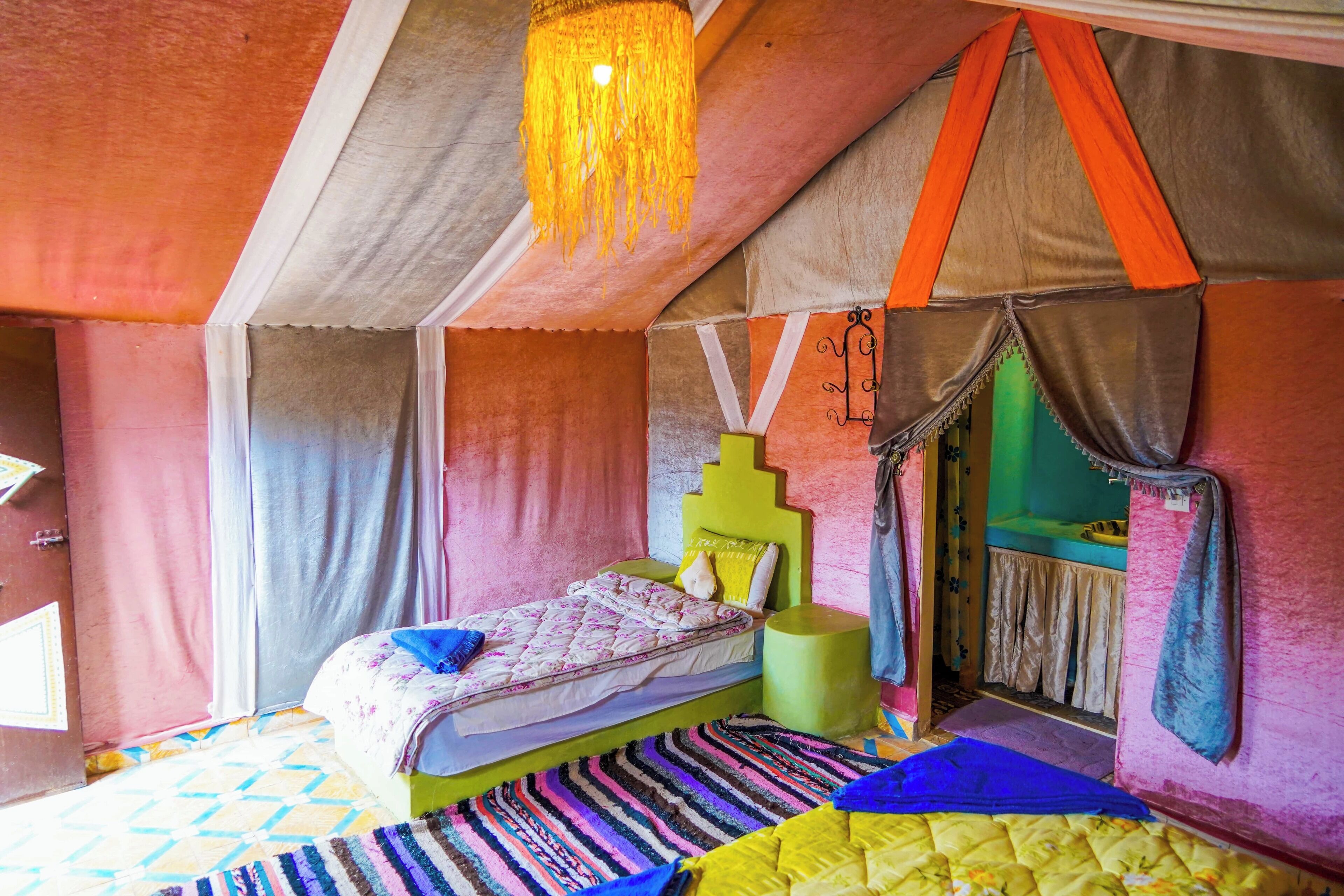 Una habitación tipo tienda de campaña, con una cama, un taburete verde y una lámpara colgante.