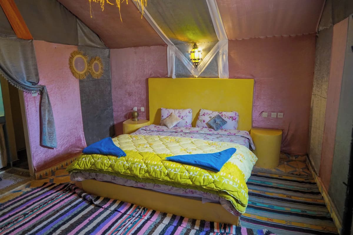 Ein Schlafzimmer mit einem gelben Kopfteil, einem Bett mit floralem Bettzeug, einem Streifen Teppich und einer hängenden Leuchte.