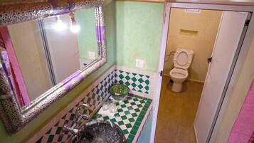 A bathroom with a green and white checkered floor, a sink with a decorative mirror, a green bowl, and a toilet.