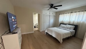 A bedroom with a bed, a TV on a stand, a ceiling fan, and a door leading to another room. - Private Hillside Pool Home with View close to Yaamava and Glen Helen  (San Bernardino)