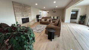 A spacious living room with a fireplace, leather sofas, a dining area, and a hallway leading to bedrooms. - Private Hillside Pool Home with View close to Yaamava and Glen Helen  (San Bernardino)