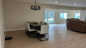 A spacious living area with a dining table, light-colored chairs, a brown sofa, and a modern chandelier. - Private Hillside Pool Home with View close to Yaamava and Glen Helen  (San Bernardino)